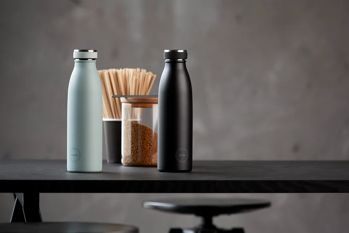 Blue and black sustainable drinking bottles from AYA&IDA on a table with coffee
